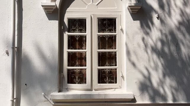 Classic arched window on a white stucco building with shifting tree shadows cast by afternoon sunlight and wind