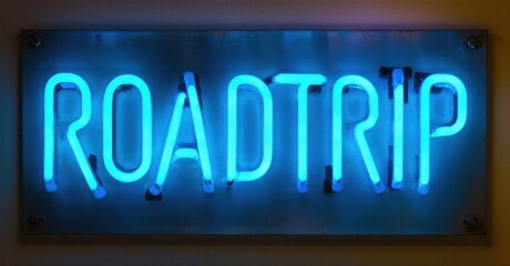 Bright neon sign displays ROADTRIP. Blue illumination against dark background. Simple typography, modern aesthetic. Wall mounted display.