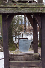 Traditional wooden water well with metal bucket and mossy roof in snowy forest setting