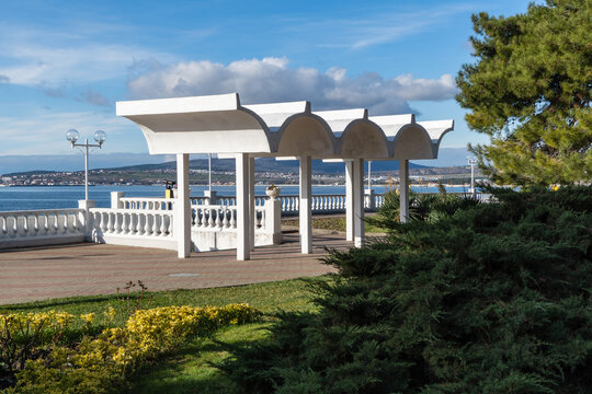 White arched pergola by seaside, surrounded by greenery, with panoramic view of coastline, distant hills and clear blue sky with scattered clouds.Gelendzhik, Russia &ndash; December 21, 2025