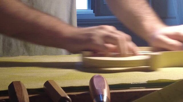 Close-up of a violin maker fitting and pressing wooden ribs onto an internal mold on a workbench, showing precision assembly and traditional luthier craftsmanship during body construction.