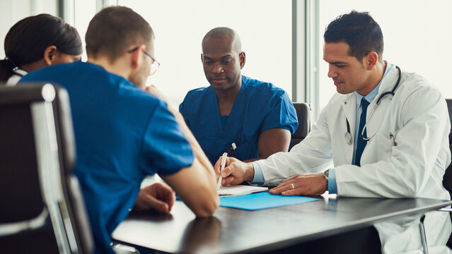 Multiracial focused medical team having a meeting in a conference room at a hospital. They take notes on a piece of paper.