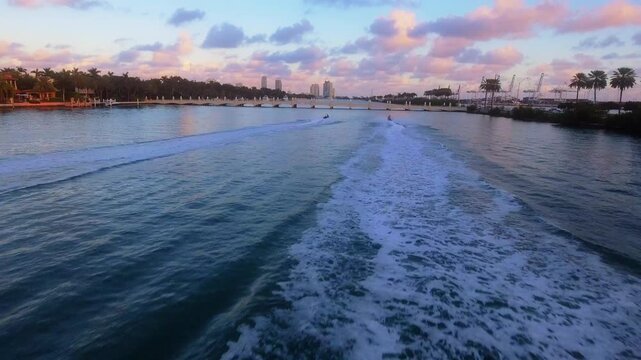 Drone follows jet skis crossing Biscayne Bay with Miami skyline during sunset.