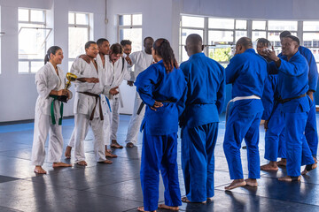 Diverse martial arts teams holding gold trophy, congratulating each other in training hall