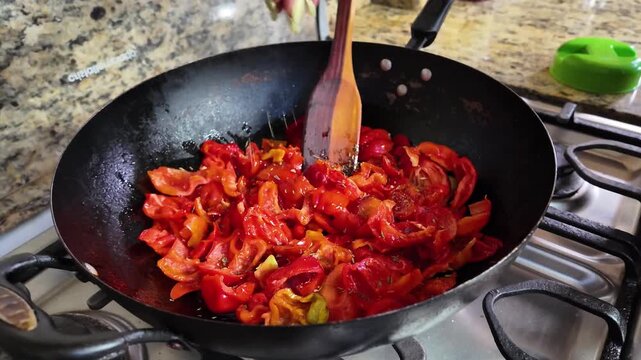 Close up of female hand seasoning red peppers in wok for sofrito meal