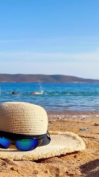 summer straw hat and sunglasses on the sand, sea and man swimming on the background, Summer vacation concept, Vertical video for social media
