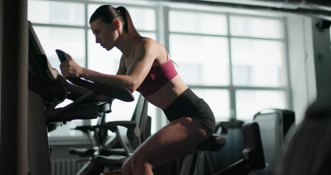A young beautiful brunette girl in sportswear exercises on a simulator in the gym doing cardio training on a stationary bike