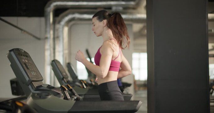 A young beautiful brunette girl in sportswear exercises on a simulator in the gym doing cardio training on a treadmill