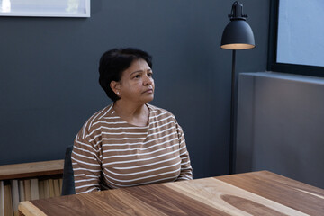Senior indian woman sitting at wooden table in meeting room, highlighting table grain