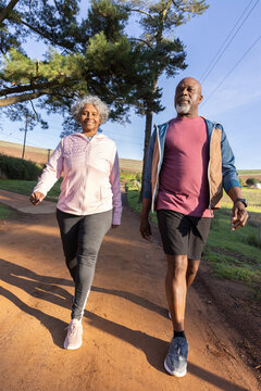 Senior couple walking on rural trail wearing hoodie vest athletic sneakers and fitness watch