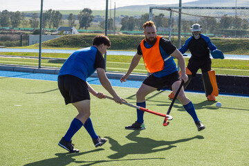 Obraz premium Male athletes in bibs and goalkeeper pads practicing hockey drill on turf with sticks and ball