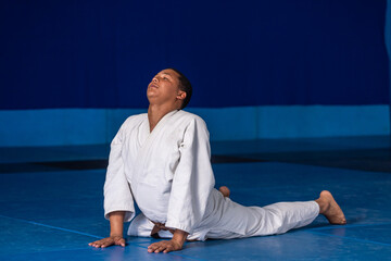 Male martial arts student performing backbend stretch in dojo on blue mat in white gi belt