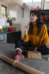 Naklejka premium Asian woman sitting in home holding cinnamon stick staring wrapping gifts with kraft paper