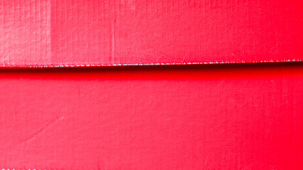 Fototapeta premium Red cardboard texture with a subtle ribbed surface and a bold horizontal shadow line from a box lid, vibrant full frame background with ample copy space