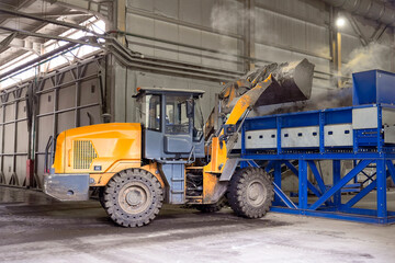 Fototapeta premium Tractor bulldozer with a bucket transports sorted small fraction waste into a container for further sorting on a conveyor belt for the production of secondary raw materials.