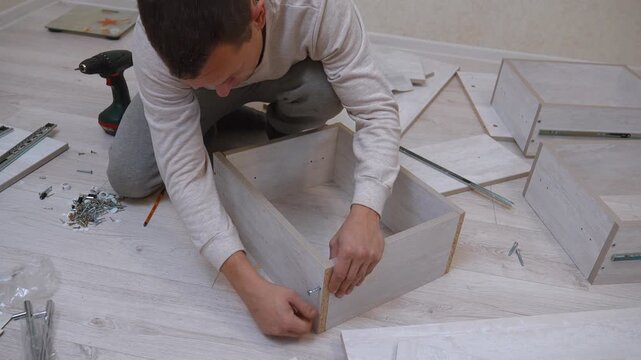 a craftsman assembles a new wooden cabinet on a laminate floor, neatly connecting the chipboard panels with screws as part of a home renovation project on his own