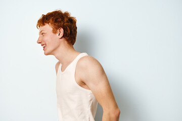 Young man with red hair wearing sleeveless shirt smiling and laughing in casual pose isolated on white background. Profile portrait of cheerful teenager with fair skin in studio. © SHOTPRIME STUDIO