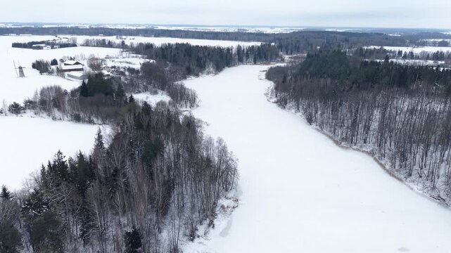 Explore this stunning drone video capturing a serene, snow-blanketed forest and river in a tranquil winter landscape. The aerial perspective showcases a peaceful, icy panorama.