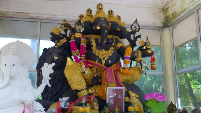 Close-up of a multi-headed and multi-armed black Ganesha statue (Phra Phikanet) seated on a lion. Adorned with flowers and sashes at Wat Nai Harn temple in Phuket, Thailand. 4K travel footage.