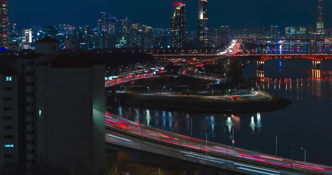 Night aerial hyperlapse pans across Seoul cityscape, heavy traffic on Gangbyeonbuk-ro expressway, ramps, illuminated Seongsu bridge over Han river revealing Lotte World Tower glowing amid skyscrapers