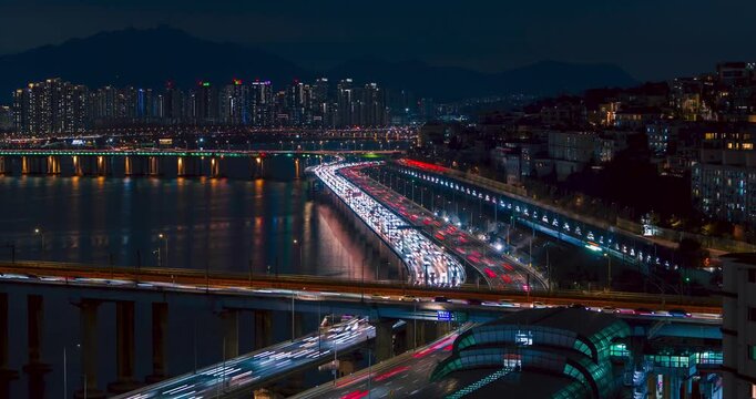 Night aerial hyperlapse zooms into Seoul cityscape showing heavy traffic on Gangbyeonbuk-ro expressway and illuminated bridges spanning Han river amid skyscrapers and mountains in Yongsan district