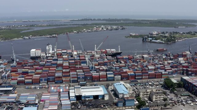 A dynamic aerial time-lapse of a bustling port, where cranes load massive container ships under a dramatic, time-compressed sky.


