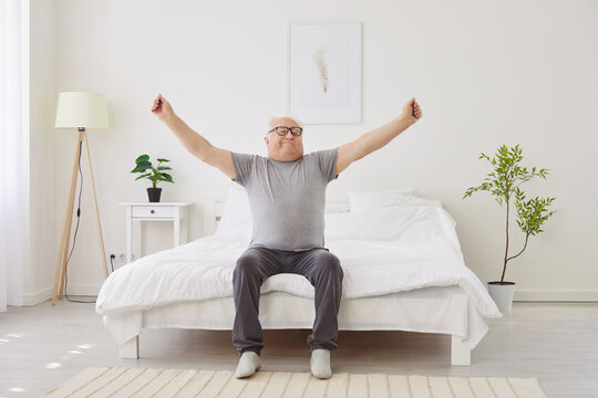 Senior man wakes up, sitting on bed and stretching to greet a new day at home. Happy and refreshed morning moment, where the man enjoys the start of his day with positivity and energy.