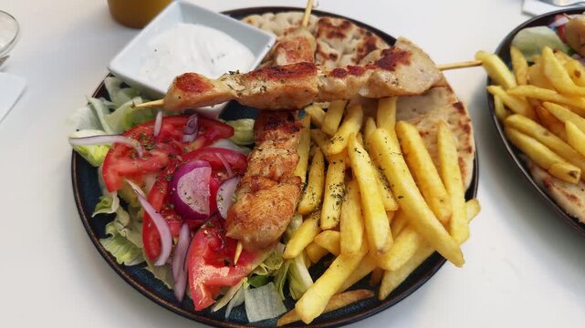 Greek pita, chicken souvlaki, green salad with fresh vegetables, French fries, and tzatziki sauce. Greek cuisine.