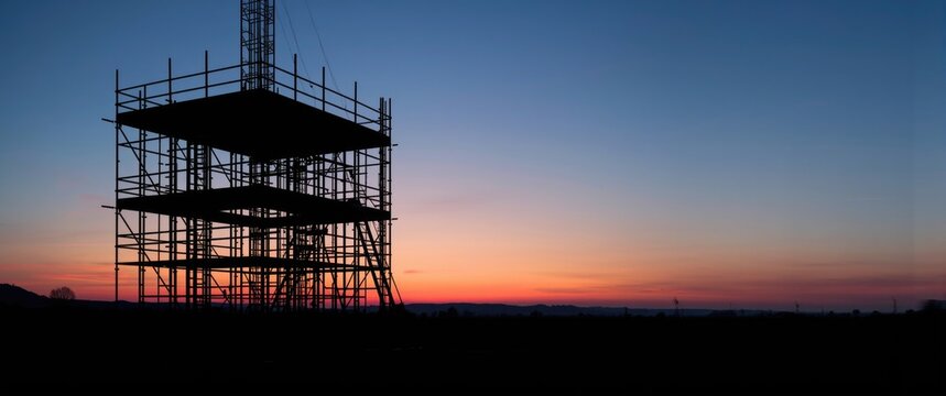 With the sun dipping below the horizon, casting a warm glow over the construction site, the scaffolding's silhouette stands tall as the dedicated crew wraps up their work