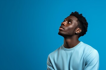 Obraz premium Young black man with dark skin looking up on a blue background, dreaming about future