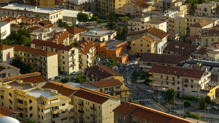 Fototapeta premium High-angle aerial close-up of a densely populated urban neighborhood, showing several multi-story residential apartment buildings with terracotta roofs, narrow streets, and small balconies.