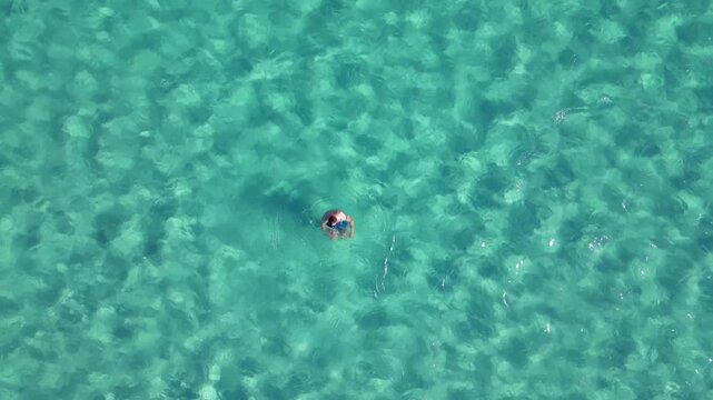 Drone top down view: man swimming in turquoise sea water showing thumb up gesture, Elafonisi pink sand beach