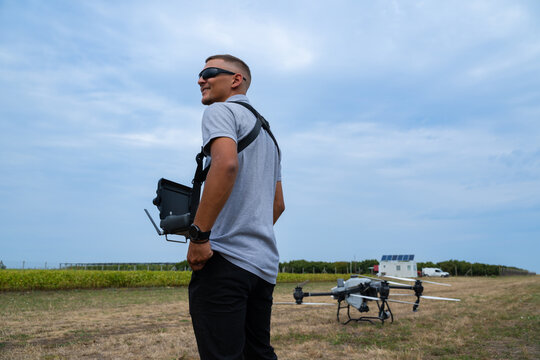 Drone pilot with controller stands in field preparing quadcopter for takeoff outdoors