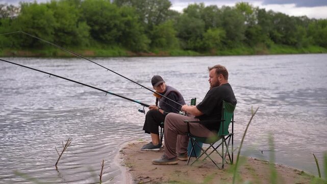 Man and woman spending quality time together, fishing with rods from the sandy bank of a river on a cloudy day, enjoying their outdoor hobby, leisure, and a quiet weekend retreat