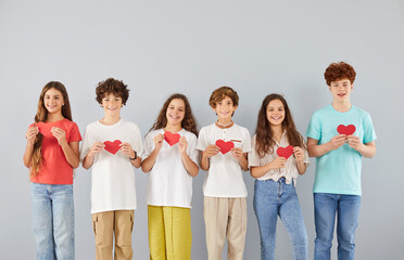 Obraz premium Studio group portrait of diverse happy smiling teenagers in casual clothes standing together in row on gray wall background, holding red paper hearts in their hands, promoting unity, love and support.