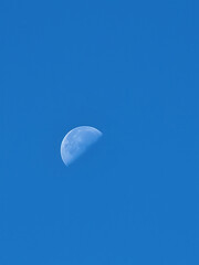 Crescent moon visible in blue daytime sky on clear sunny day