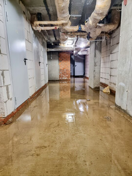 Flooded basement corridor with utility pipes and concrete walls