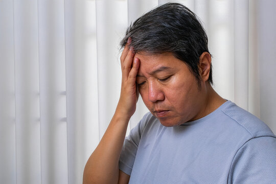 Middle-aged Asian man experiencing a headache, for a healthcare and medical project.