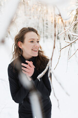 Smiling brunette woman in black ski suit standing in winter forest 