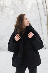 Smiling woman in black outerwear looking away in winter forest 