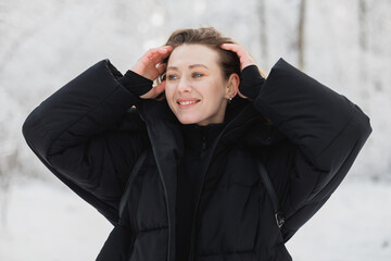 Cheerful woman in black outerwear standing in winter forest 