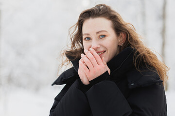 Portrait of smiling woman warming hands and looking at camera in winter forest 