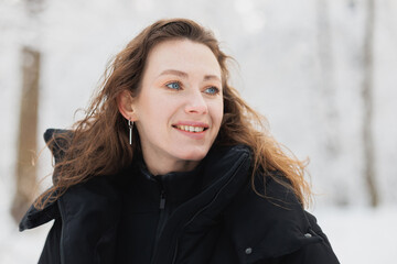 Portrait of curly woman smiling in winter forest 