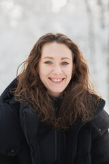 Portrait of happy woman in outerwear looking at camera in winter forest 