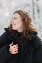 Portrait of cheerful woman in outerwear jacket in winter forest 