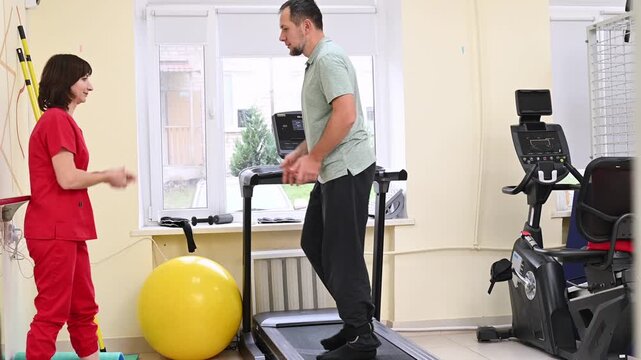 A man recovers from an injury on a treadmill under the guidance of a physical therapist. Stroke rehabilitation, physical activity. Restoration of brain functions and motor coordination