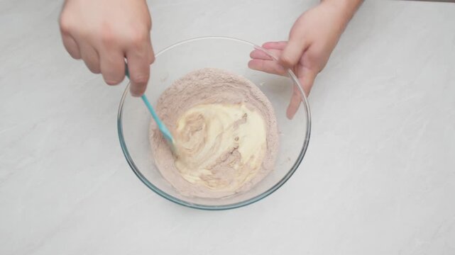 Top down view of cream being folded into a cocoa mixture using a spatula in a glass bowl