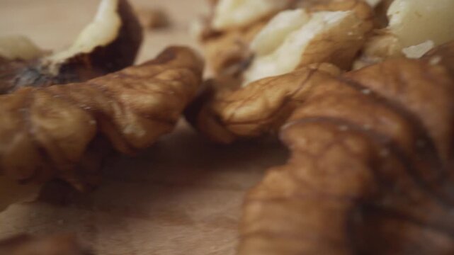 Extreme close-up of a pile of shelled walnuts appearing and disappearing on a textured wooden board. Healthy eating and nutritious food concepts