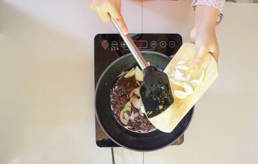 Chef putting fresh sliced onions into a frying pan with savory sauce