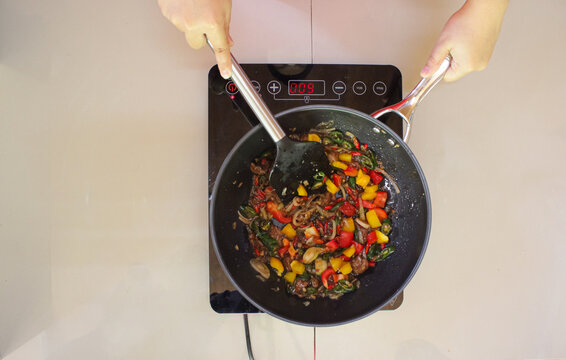 Person cooking delicious beef black pepper with colorful bell peppers in a wok